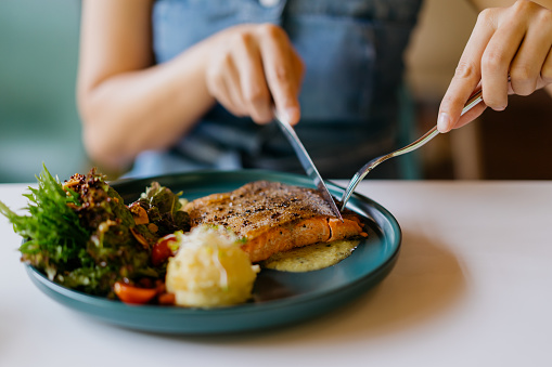 Asian woman eating pan fried salmon in cafe