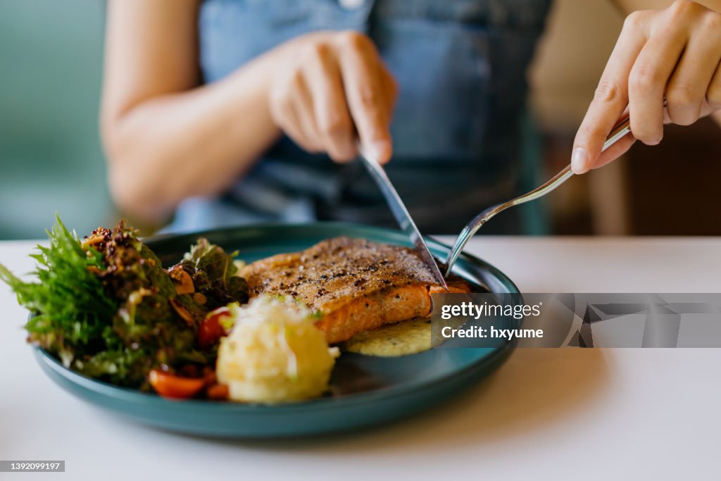 Asian woman eating pan fried salmon in cafe