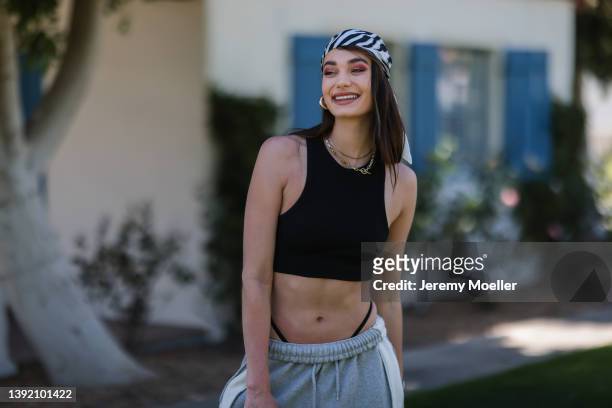 Sarah Posch seen wearing a satin scarf with zebra print as a hair accessory/bandana, a black crop top, gold earrings and necklaces and a grey...