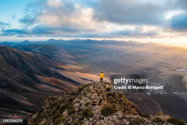 man standing on top  of a cliff looking at sunset, lanzarote, spain - natural landmark stock-fotos und bilder