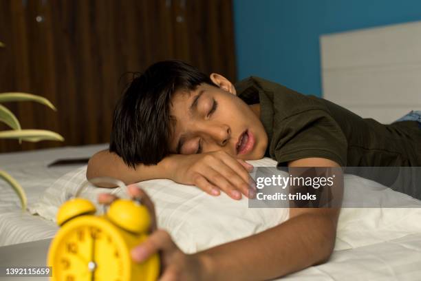 ragazzo che si avvicina per spegnere la sveglia mentre dorme sul letto - bocca aperta foto e immagini stock