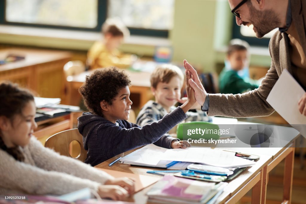 Happy teacher and schoolboy giving each other high-five on a class.