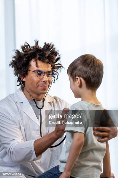 a male doctor of african ethnicity is using his stethoscope to listen to his young patient's chest. - child listening differential focus stock pictures, royalty-free photos & images