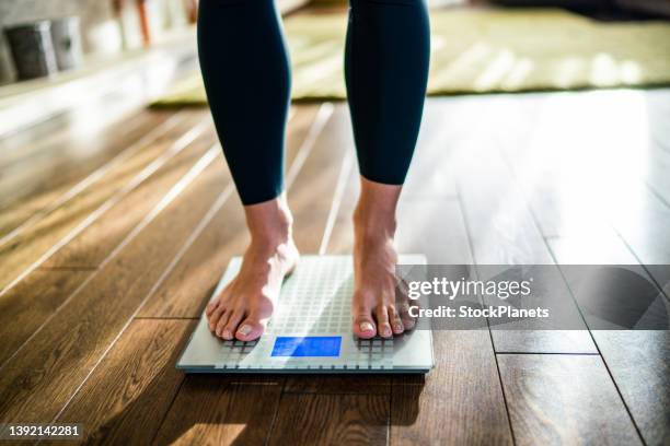 female is checking her weight on the scale - weegschaal weeginstrument stockfoto's en -beelden