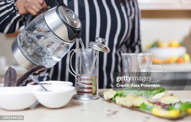 tea making. black woman makes traditional herbal tea, pouring hot water into a french-press. close-up photo with hands only. - coffee plunger stock pictures, royalty-free photos & images