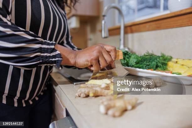 お茶作り。伝統的なハーブティーのために生姜を刻むアフリカ系アメリカ人女性。手だけでのクローズアップ写真。 - ショウガ ストックフォトと画像