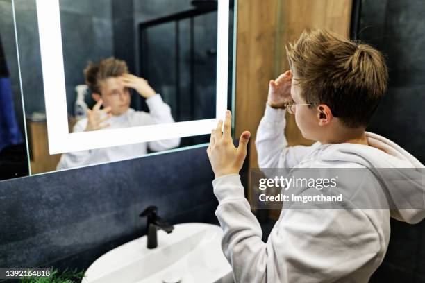teenage boy styling his hair in the morning in the dark blue bathroom. - combing stockfoto's en -beelden
