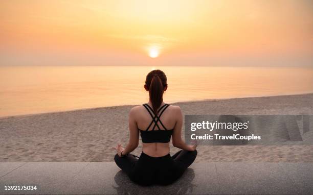 young healthy woman practicing yoga on the beach at sunset. body of beautiful girl in a meditation on the beach. lifestyle woman yoga exercise and pose for healthy life. welness background. spa concept. - lotuspositie stockfoto's en -beelden