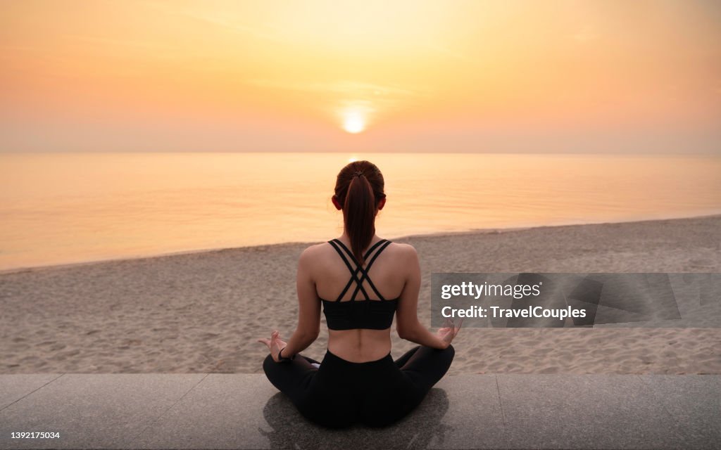 Young healthy woman practicing yoga on the beach at sunset. Body of beautiful girl in a meditation on the beach. Lifestyle woman yoga exercise and pose for healthy life. Welness background. Spa concept.