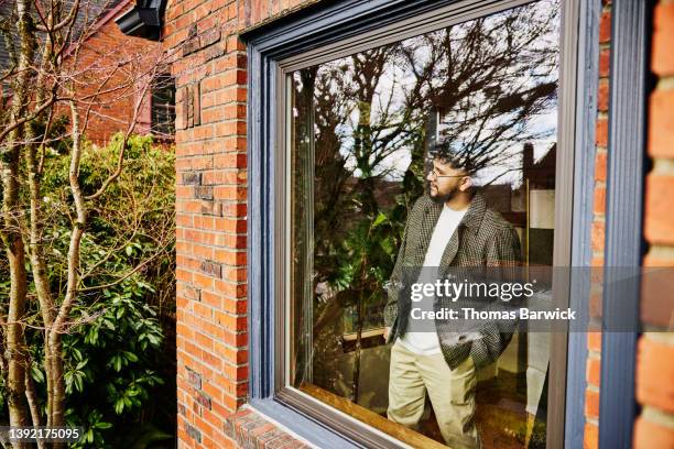 medium wide shot exterior view of man looking through window of home - home sweet home stockfoto's en -beelden