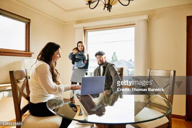 medium wide shot of family in discussion with real estate agent in home for sale - conference dining table stockfoto's en -beelden