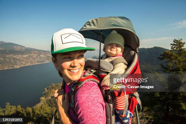 a young woman stands atop a mountain with a baby in a backpack - baby lachen natur stock-fotos und bilder