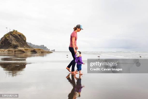 a young woman walks with a young child on a vast empty beach - hot women on boats stock pictures, royalty-free photos & images