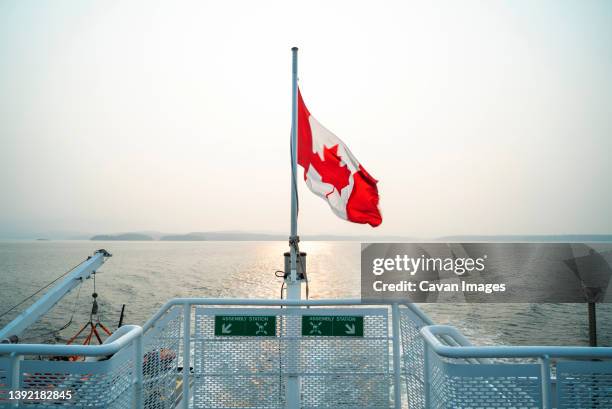 canadian flag waves at stern of ferry boat over water - british columbia flag stock pictures, royalty-free photos & images