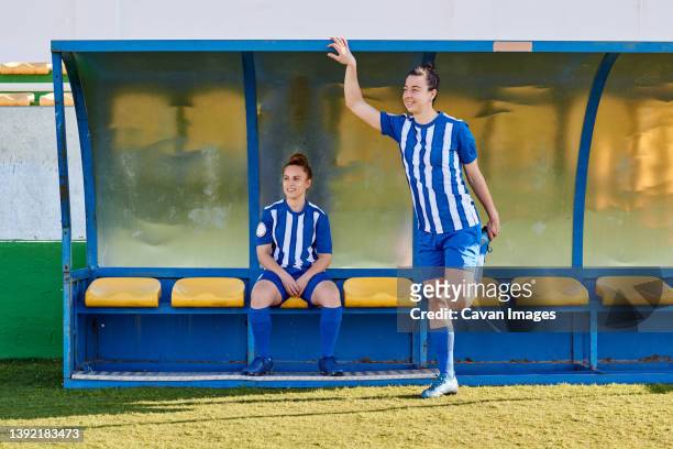 two women soccer players look out over the soccer field from the bench - football bench stock pictures, royalty-free photos & images
