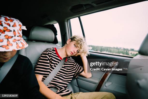 bored kids passing time in the backseat on a road trip - desinteresse stock-fotos und bilder