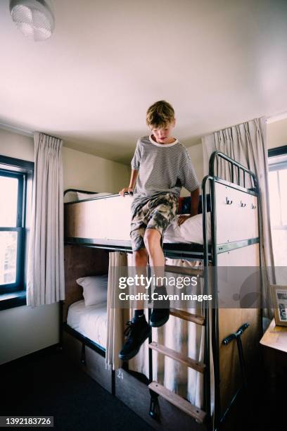 teen boy slides down from bunkbed in hostel - kids in bunk bed stock pictures, royalty-free photos & images