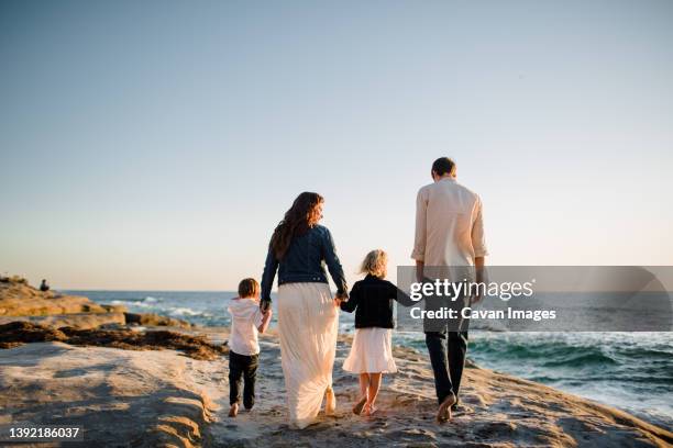 family of four walking along cliff on beach at sunset in san diego - san diego california beach stock pictures, royalty-free photos & images