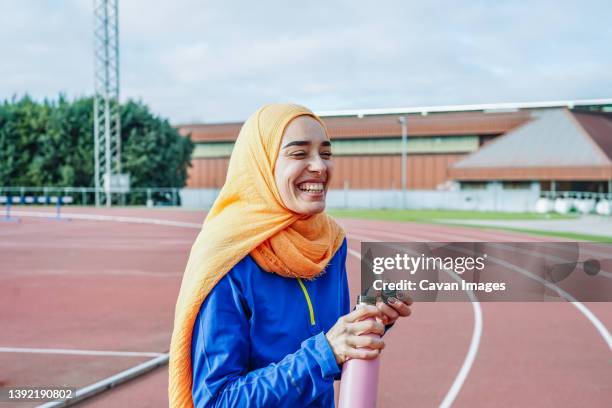 joyful ethnic woman drinking water from bottle on racetrack - funny muslim stock pictures, royalty-free photos & images