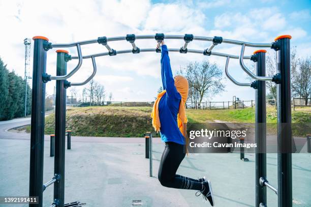 islamic woman hanging on monkey bar on sports ground - monkey bars stock pictures, royalty-free photos & images