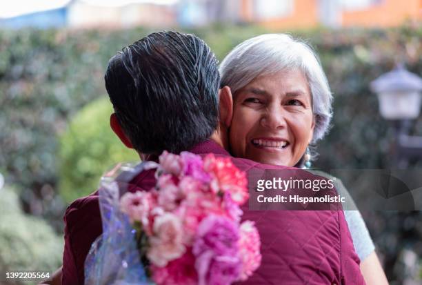 unrecognizable man hugging his mom celebrating mother's day giving her a flower bouquet - colombia flowers stock pictures, royalty-free photos & images