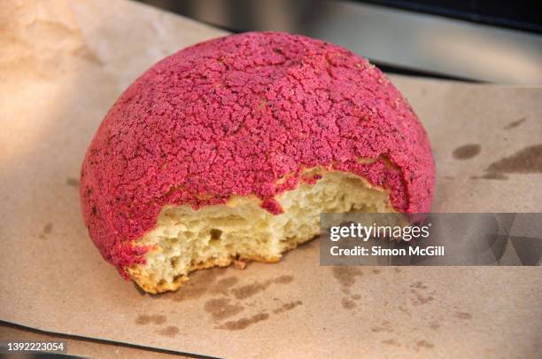 jamaica/hibiscus flavored concha sweet bun with a missing bite on a brown paper bag - sweet bread stock pictures, royalty-free photos & images