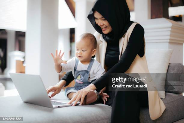 mother holding her baby when working from home - muslim boy stockfoto's en -beelden