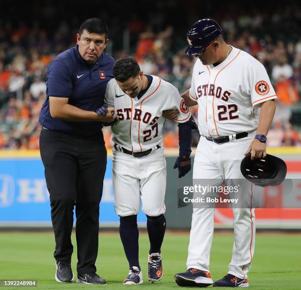 Jose Altuve of the Houston Astros is helped off the field by first base coach Omar Lopez and a trainer after injuring himself running out an infield...