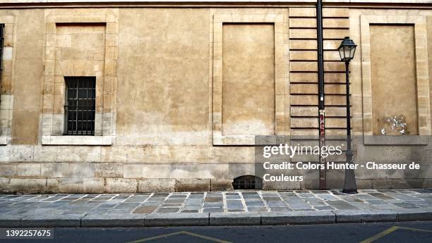 empty street in paris with weathered wall, cobblestone sidewalk with antique street lamp - trottoir photos et images de collection