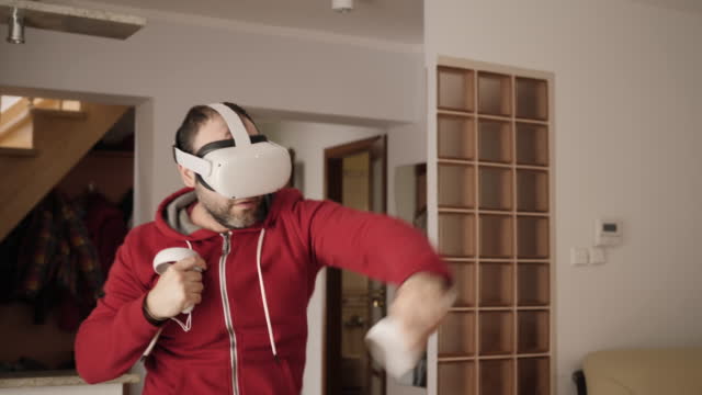 Man At Home Wearing Virtual Reality Headset Holding Gaming Controllers. Active VR Game Virtual Reality Technology Gaming Simulation Helmets. Person Fight Boxing AR Glasses. Metaverse Oculus Technology
