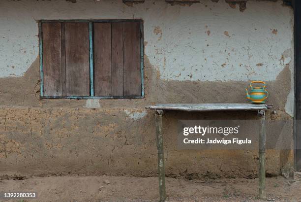 a wooden table stands in front of the mud house in remote village in liberia. - マッドハット ストックフォトと画像