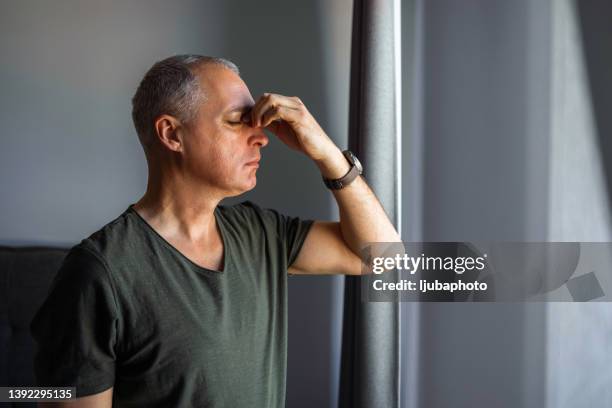 depressed man standing by the window i - sinus headache stock pictures, royalty-free photos & images