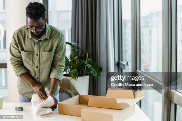 young man unboxing online purchase in the living room - returning goods stock pictures, royalty-free photos & images