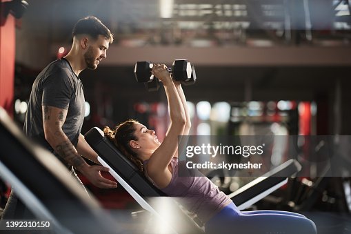Joven ayudando a su novia durante su entrenamiento deportivo en un club de salud. Joven ayudando a su novia durante su entrenamiento deportivo en un club de salud.