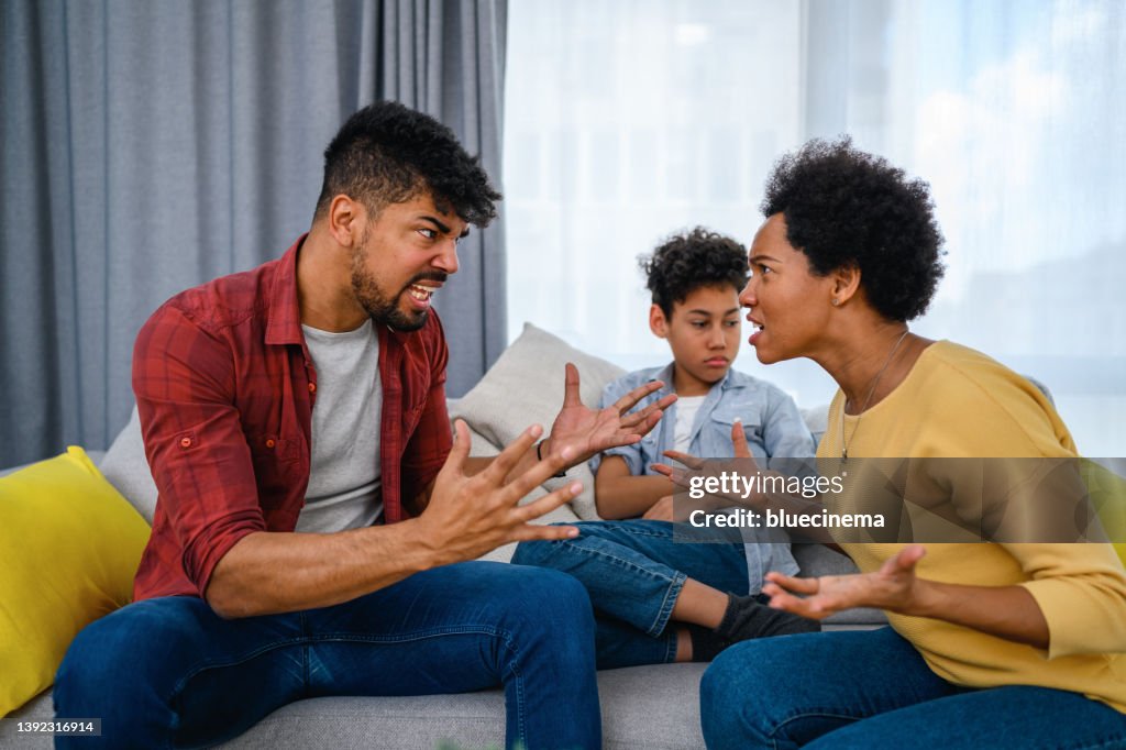 Parents arguing while the son is sitting between them at home.