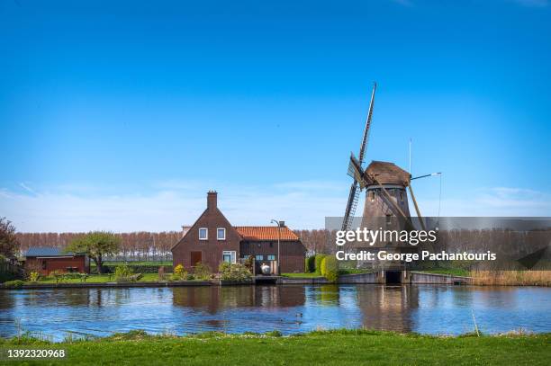 traditional dutch windmill and house next to the river - mill bank stock pictures, royalty-free photos & images