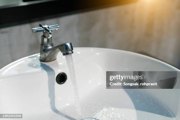 shot of an open tap with running water in a bathroom at home - vattenhushållning bildbanksfoton och bilder