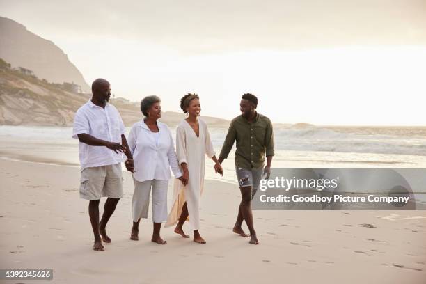 smiling senior couple and their daughter and son-in-law walking on a beach - family trip in laws stock pictures, royalty-free photos & images