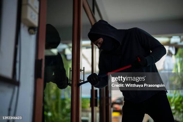 one man, criminal dressed all in black with crowbar, breaking in through window in house. - burglary stock pictures, royalty-free photos & images