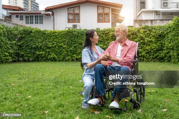 female healthcare talking to a senior man in a wheelchair while relaxing in the backyard. - infirmière et maison photos et images de collection