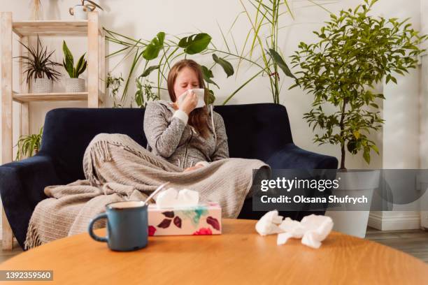 sick woman sitting on the couch - sick woman blowing nose stock pictures, royalty-free photos & images