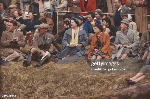 Queen Elizabeth II and the Queen Mother sitting on the ground to watch the Badminton Horse Trials, 1956. On the Queen's other side is Mary, Countess...
