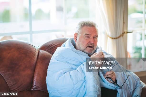ill senior man blowing his nose with a tissue at home - snuit stockfoto's en -beelden