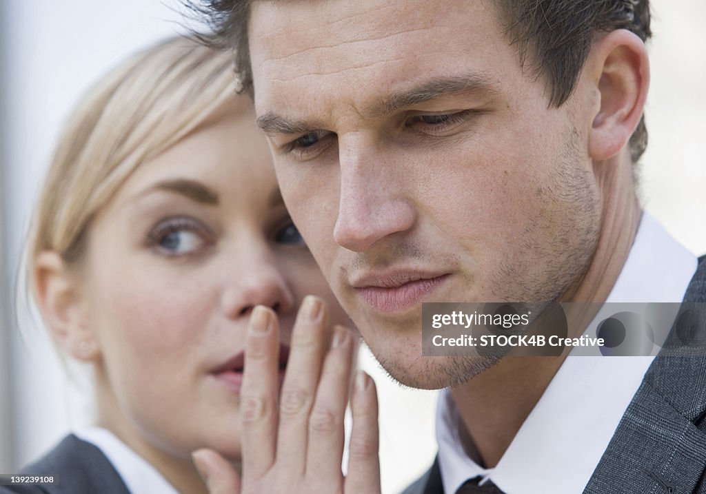 Businesswoman whispering to businessman