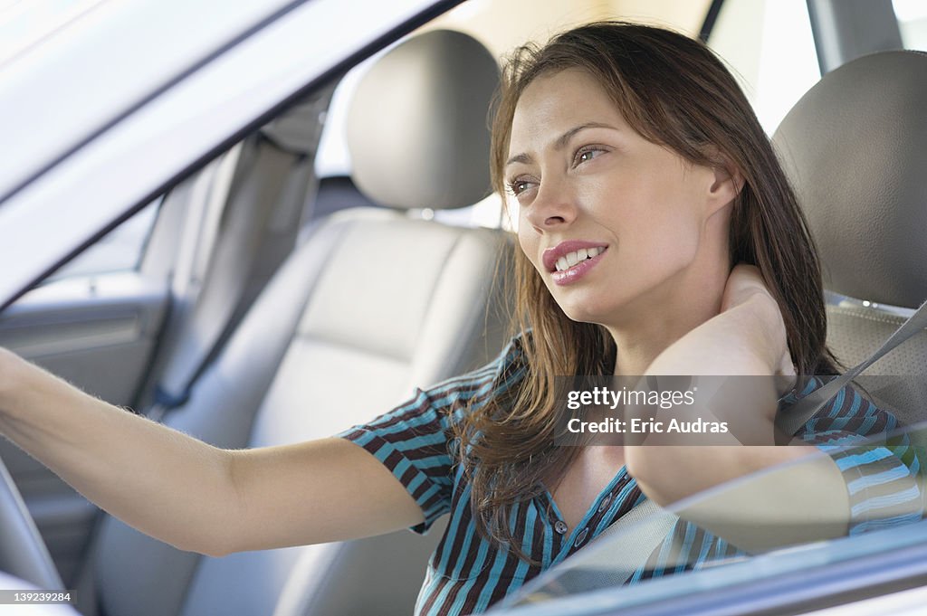 Tired young woman rubbing back of neck while driving a car