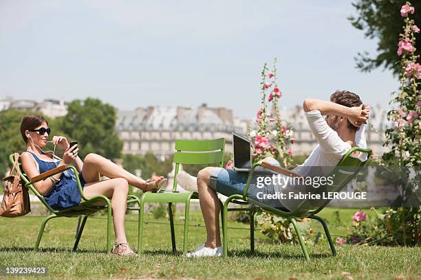 man using a laptop with a woman talking on a mobile phone, jardin des tuileries, paris, ile-de-france, france - french garden stock-fotos und bilder