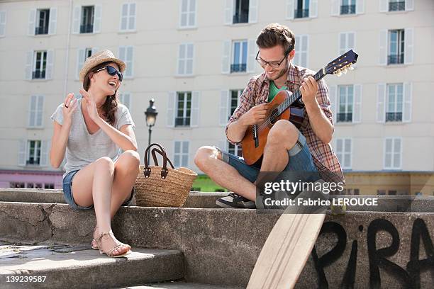 man playing a guitar with a woman clapping and smiling, canal st martin, paris, ile-de-france, france - martin guitar stock pictures, royalty-free photos & images