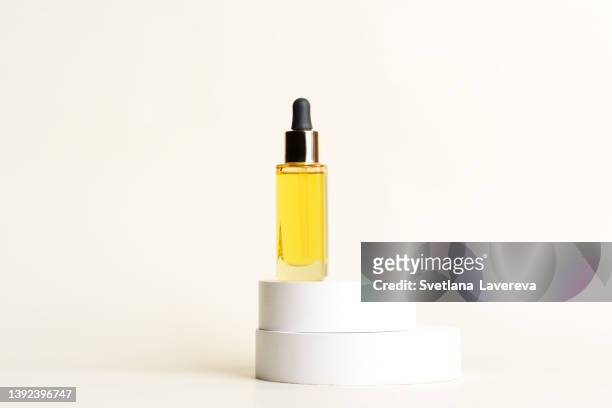 a glass dropper bottle with a pipette with black rubber tip on the white round circle podiums on the light beige background. nature skin concept. organic spa cosmetics. trendy concept. - flacon compte gouttes photos et images de collection