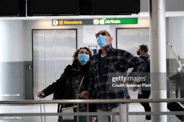 Travelers wearing masks look up at a sign inside John F. Kennedy Airport on April 19, 2022 in New York City. On Monday, a federal judge in Florida...