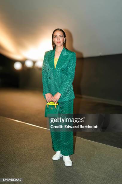 Monia Chokri wears earrings, a golden necklace, a yellow Gucci ribbed top, a green shiny Gucci monogram-printed blazer jacket, matching suit pants, a...